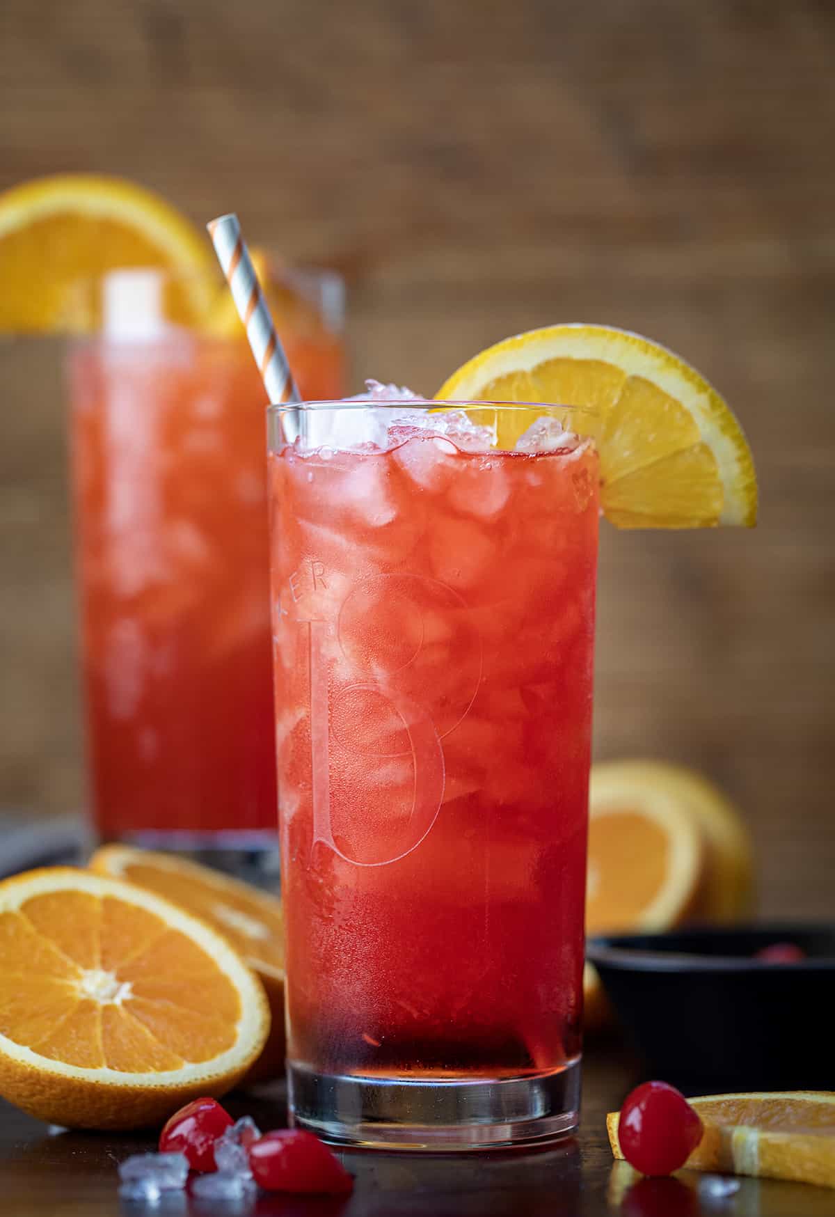 Alabama Slammer is an alcoholic beverage made with Southern Comfort, sloe gin, amaretto, and orange juice, shaken and poured over a glass of crushed ice. Top off the drink with orange slices and maraschino cherries for garnish. It is a refreshing cocktail that can also be served as a shot! Alabama Slammer Cocktail on a Cutting Board with Oranges and a Straw.