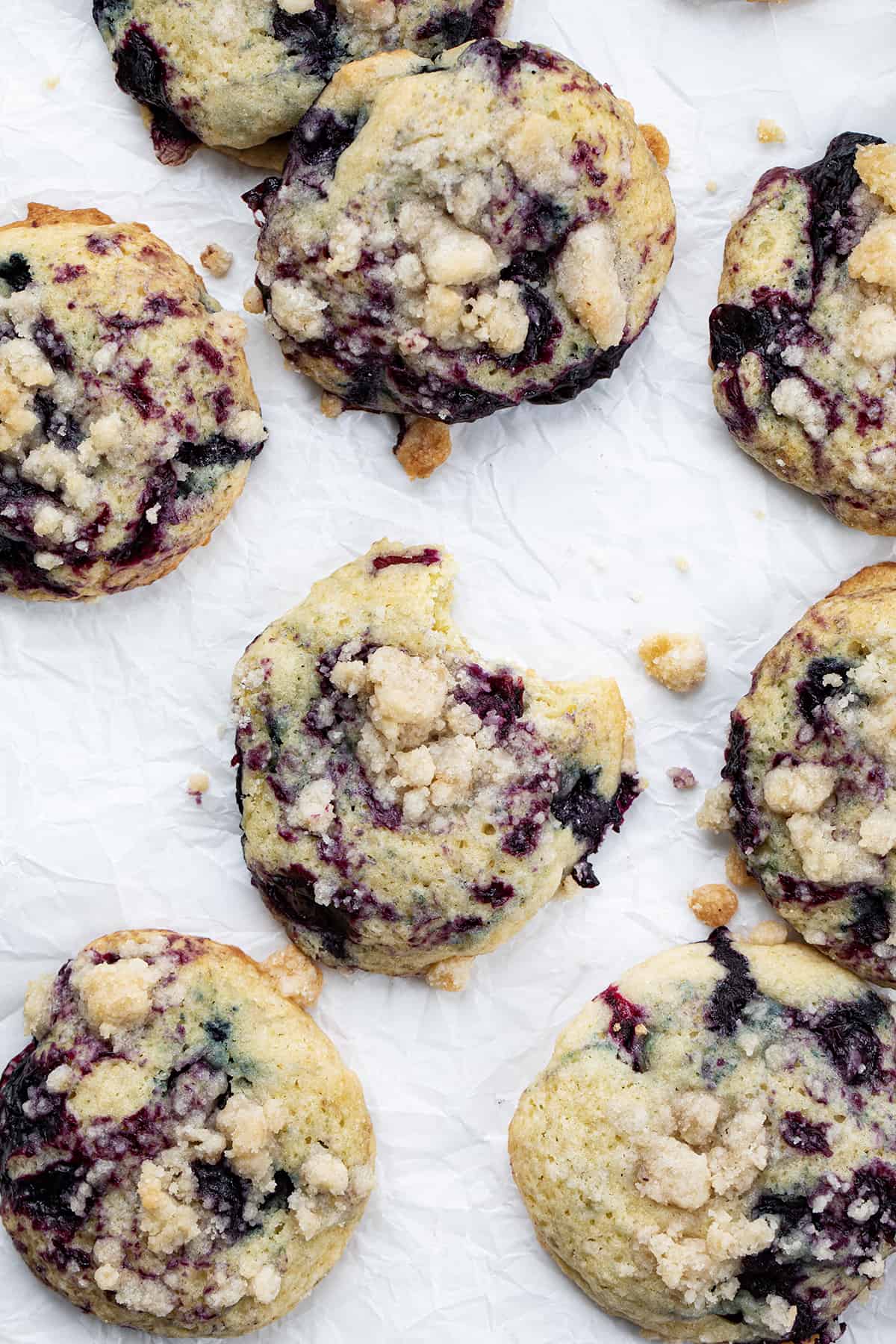 Blueberry Crumble Cake Cookies are soft, cake-like cookies with blueberry filling swirled inside and topped with a crumble topping. They are a delightful treat that combines the tenderness of a muffin or cake with the irresistible texture of a crumbly topping. They are truly a heavenly delight for blueberry lovers. Blueberry Crumble Cake Cookies with Center Cookie Having a Bite Taken Out.