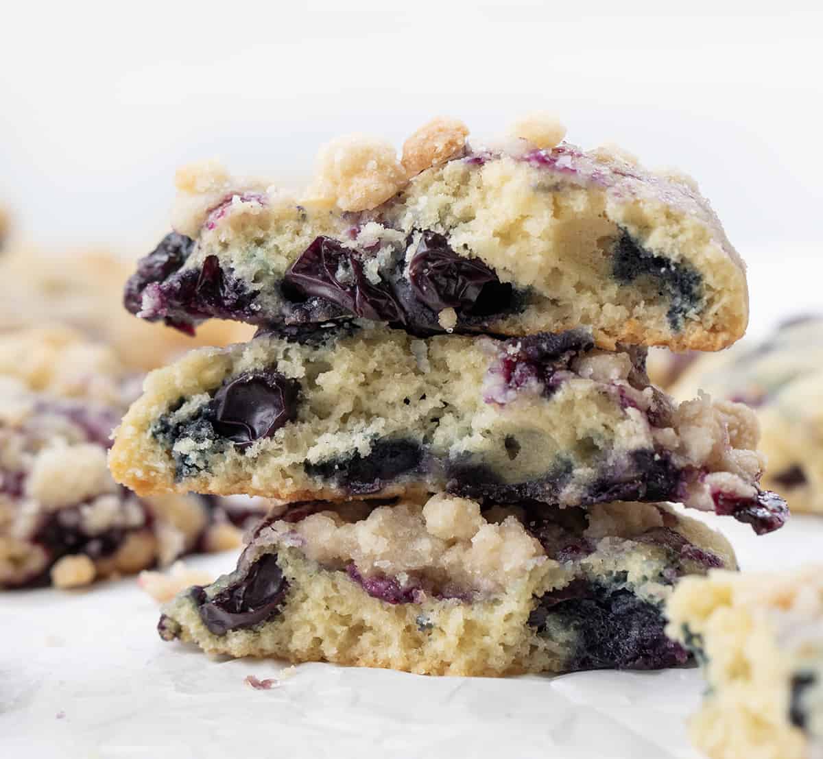 Blueberry Crumble Cake Cookies are soft, cake-like cookies with blueberry filling swirled inside and topped with a crumble topping. They are a delightful treat that combines the tenderness of a muffin or cake with the irresistible texture of a crumbly topping. They are truly a heavenly delight for blueberry lovers. Blueberry Crumble Cake Cookies Broken in Half and Stacked, Showing Inside Texture.
