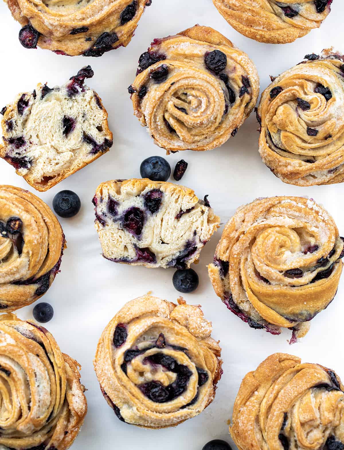 Blueberry Cruffins will be your new favorite blueberry treat! They are made with fresh blueberries rolled into crescent roll sheets and then baked. It's layer after layer of soft dough bursting with blueberries in every bite! Blueberry Cruffins on a White Counter with Most Whole and One Cut in Half.