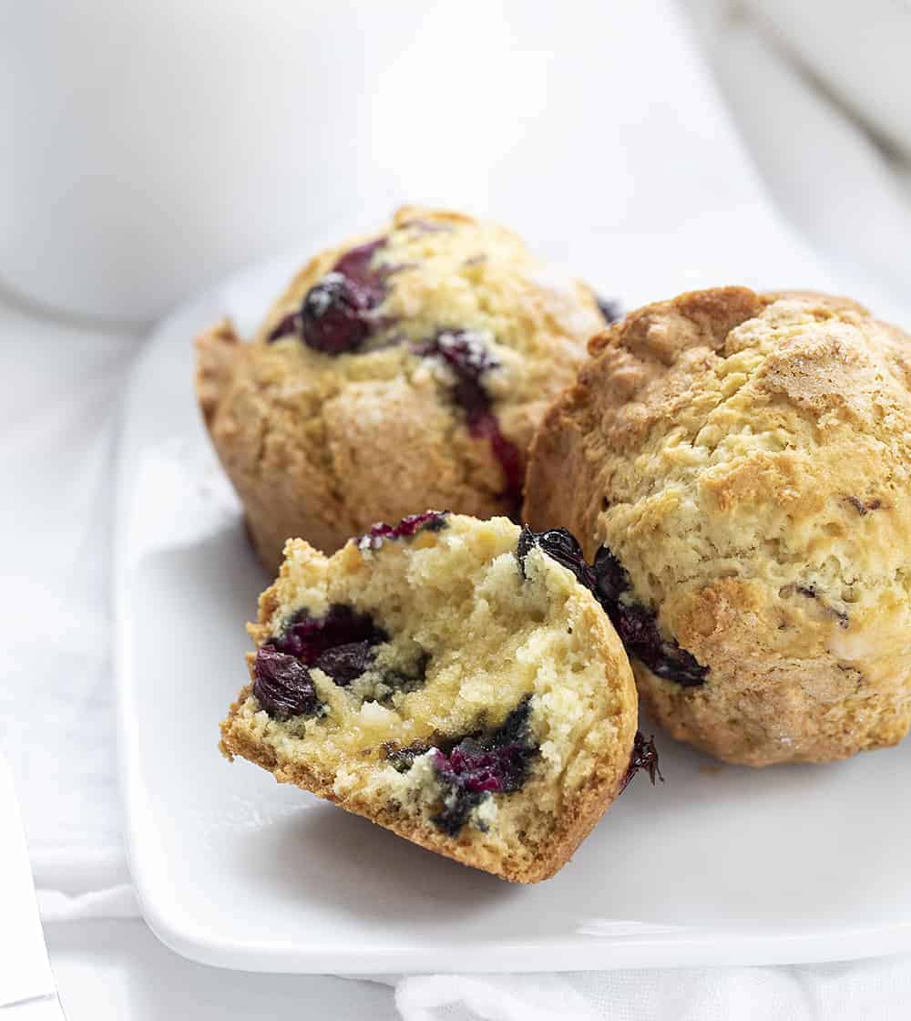 Use your sourdough starter to make these moist and fluffy Sourdough Blueberry Muffins. sourdough blueberry muffins, blueberry muffins, muffins recipes, blueberry recipes, breakfast, iambaker, i am baker, sourdough starter White Plate with Sourdough Blueberry Muffins and One Torn in Half with Butter