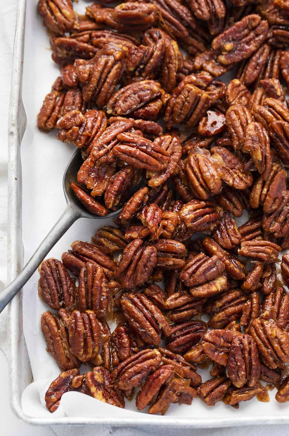 Candied Pecans are a sweet and crunchy treat that is easy to mix together and bake anytime you need to satisfy a sweet tooth! Candied Pecans, How to Make Shiney Candied Pecans, Perfect Candied Pecans, iambaker, i am baker, recipes, Christmas, baking, holidays, appetizer Overhead of Candied Pecans in Pan with Spoon