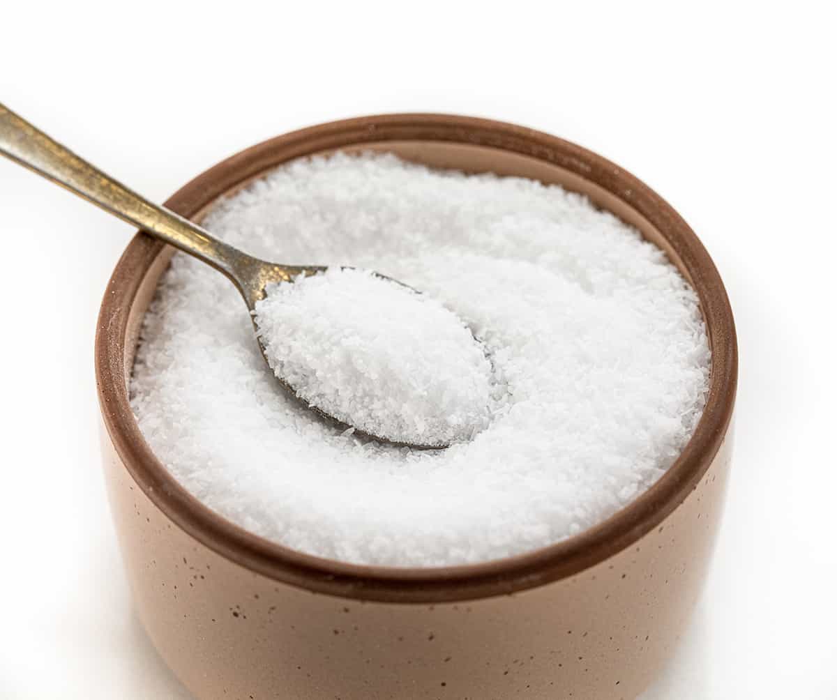 I often get asked about the role of salt in baking, especially kosher as that is what I prefer. Salt is not just a flavor enhancer, but it also plays a vital role in the baking process. In fact, it's one of the four essential ingredients in bread - flour, salt, yeast, and water. I'd love to share which salt I use, and why different salts can't be used interchangeably! A Container of Kosher Salt with a Spoon in it.
