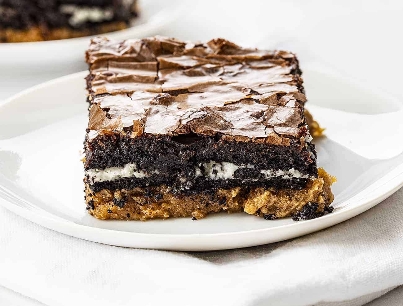 Peanut Butter Slutty Brownies are a decadent dessert that starts with a layer of a peanut butter cookie, followed by a layer of double-stuffed Oreo cookies and topped with chocolate brownie! Slutty Brownies, Oreo Brownies. Peanut Butter Slutty Brownies, How to Make Slutty Brownies, Variations of Slutty Brownies, Easy Slutty Brownies. Chocolate Brownies, i am baker, baking, recipes, brownies, iambaker Peanut Butter Slutty Brownies on White Plate on White Napkin