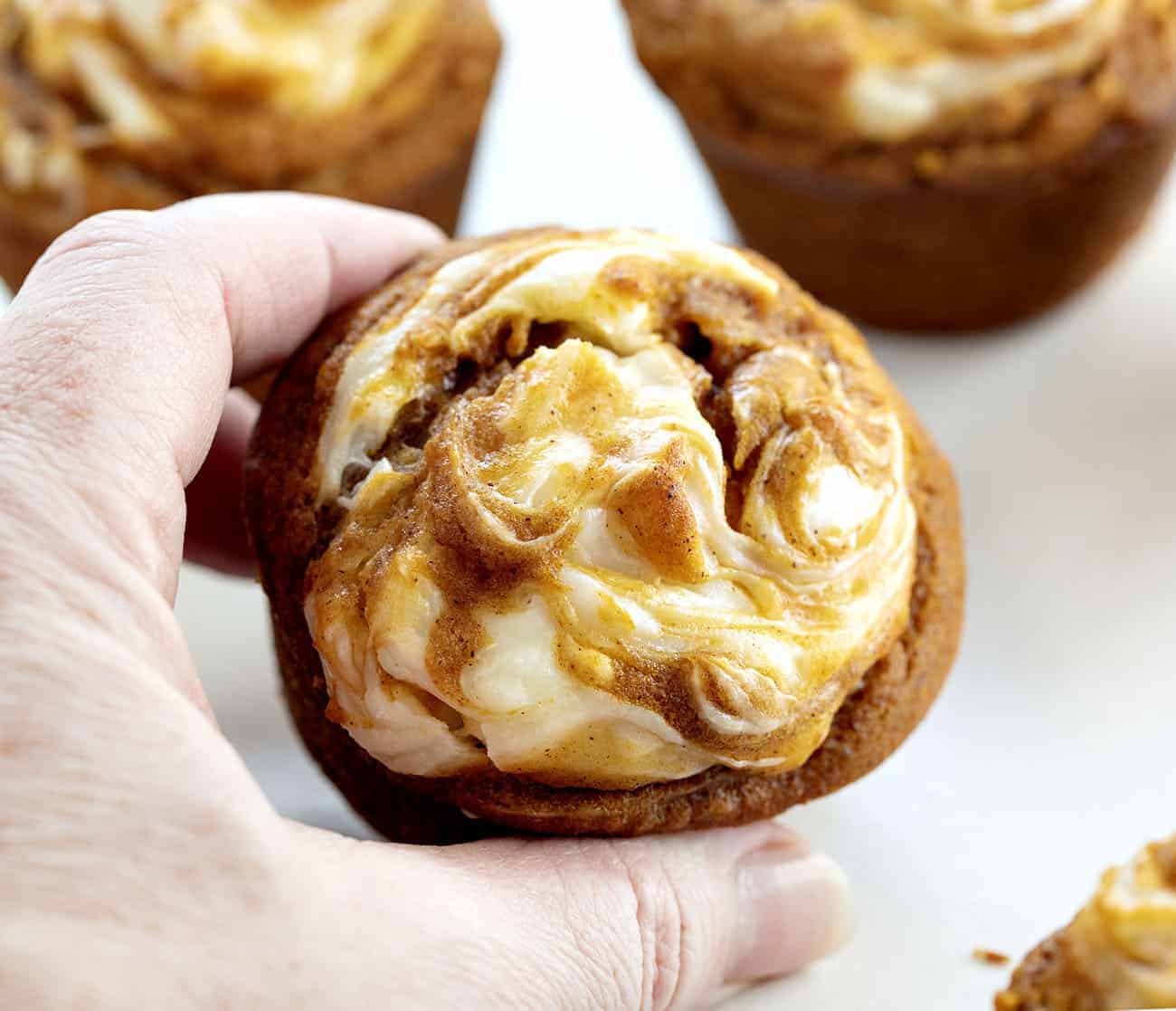 With a cream cheese swirl and a perfectly moist pumpkin muffin, Pumpkin Cream Cheese Swirl Muffins are the best thing about pumpkin spice season! #pumpkincreamcheeseswirlmuffins #muffinrecipes #pumpkinmuffins #iambaker #homemadepumpkinspice #pumpkinspice #baking #desserts #creamcheesefilledmuffins Hand Holding Pumpkin Cream Cheese Swirl Muffin