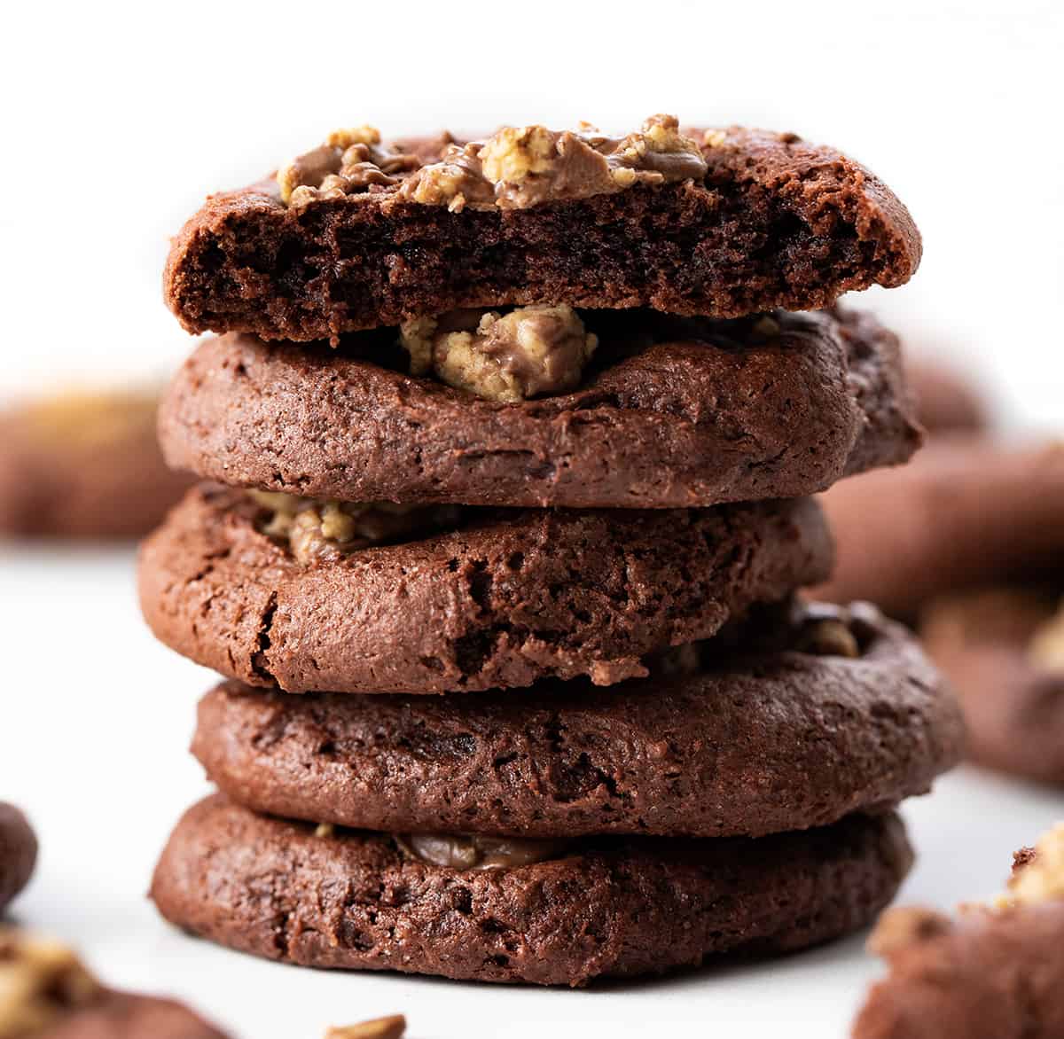 Chocolate Reese's Cake Mix Cookies are cookies made with chocolate cake mix and topped with chopped mini Reese's peanut butter cups. I love from-scratch cookies (there are hundreds on my website!) but also love the convenience of grabbing a cake mix! Stack of Reese's Cake Mix Cookies with Top Cookie Broken Showing the Inside.