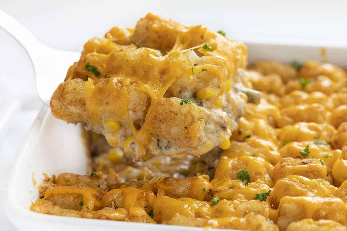 Tater Tot Hotdish is a quick and easy comfort food staple recipe all over the Midwest! This hotdish is full of meat, veggies, soup, cheese, and topped with tater tots for a super satisfying meal! Tater Tot Hotdish, Tater Tot Casserole, How to Make Hotdish, Casserole, Tater Tot Recipes, Dinner, Supper, Recipes, Dinner Ideas, Midwest Recipes, i am baker, iambaker Spatula with Tater Tot Hotdish on it and Ooey Gooey Cheese on Top