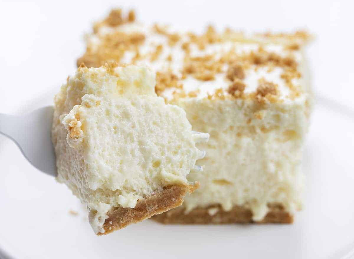 Woolworth Icebox Cheesecake Recipe is a light and fluffy, no-bake dessert with a hint of lemon flavor on top of a graham cracker crust. Woolworth Recipe, Cloud Cheesecake, Icebox Cake, BBQ, Summer Desserts, Dessert, Old Fashioned Dessert, Vintage Cake, i am baker, iambaker Fork Holding Bite of Woolworth Icebox Cake Recipe